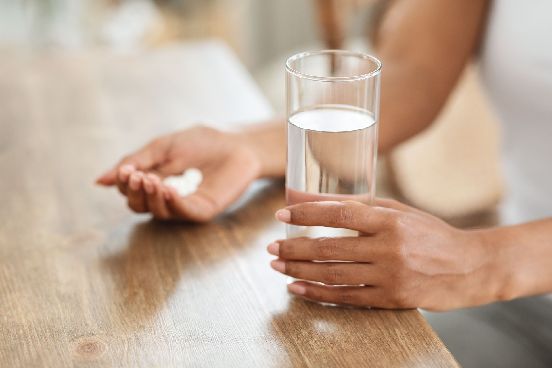 Unrecognizable black woman takes medicines with glass of water at home